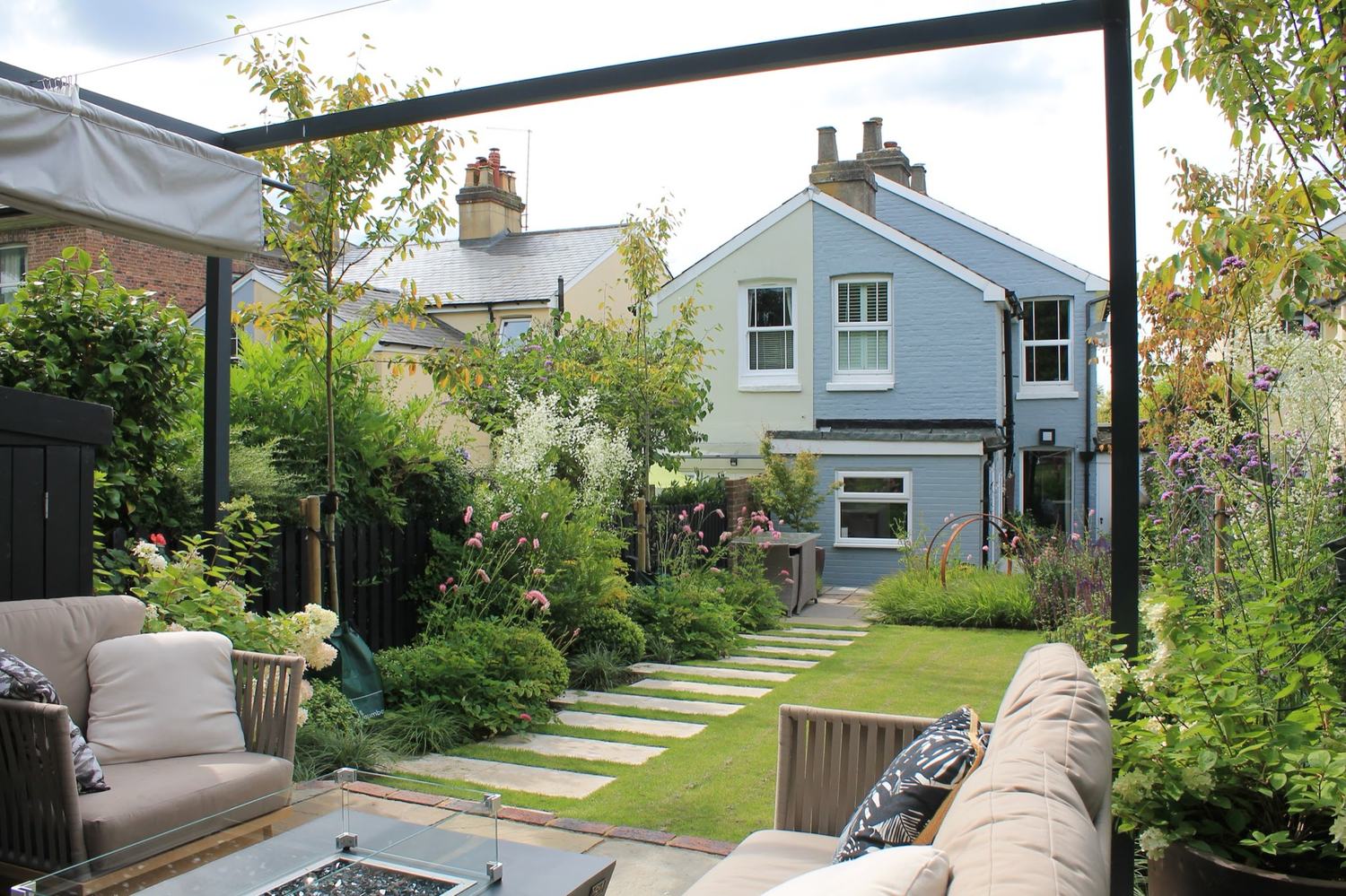 Stepping stones crossing a small lawn towards the house, seen from a covered seating area — the layout giving the garden a route, a destination and somewhere to sit at either end of it.